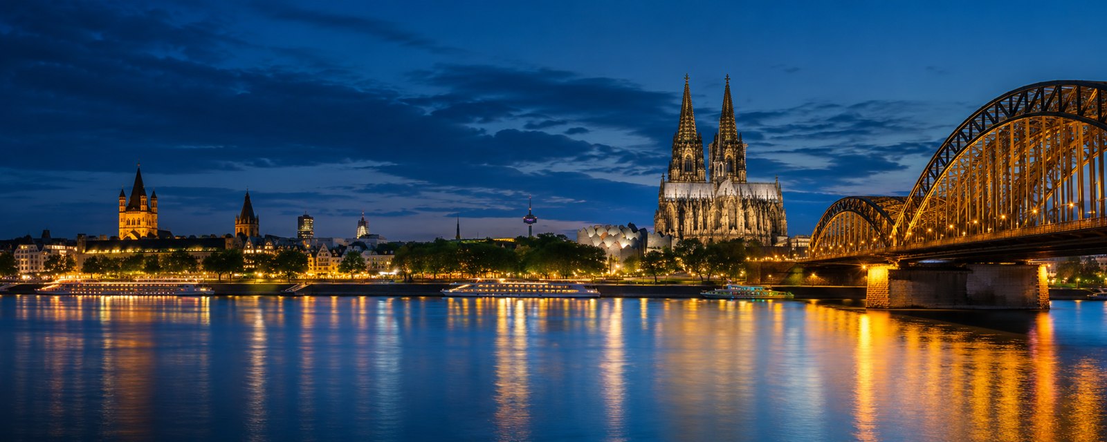 Illustratives Rheinpanorama mit Kölner Dom und beleuchteter Brücke zur blauen Stunde
